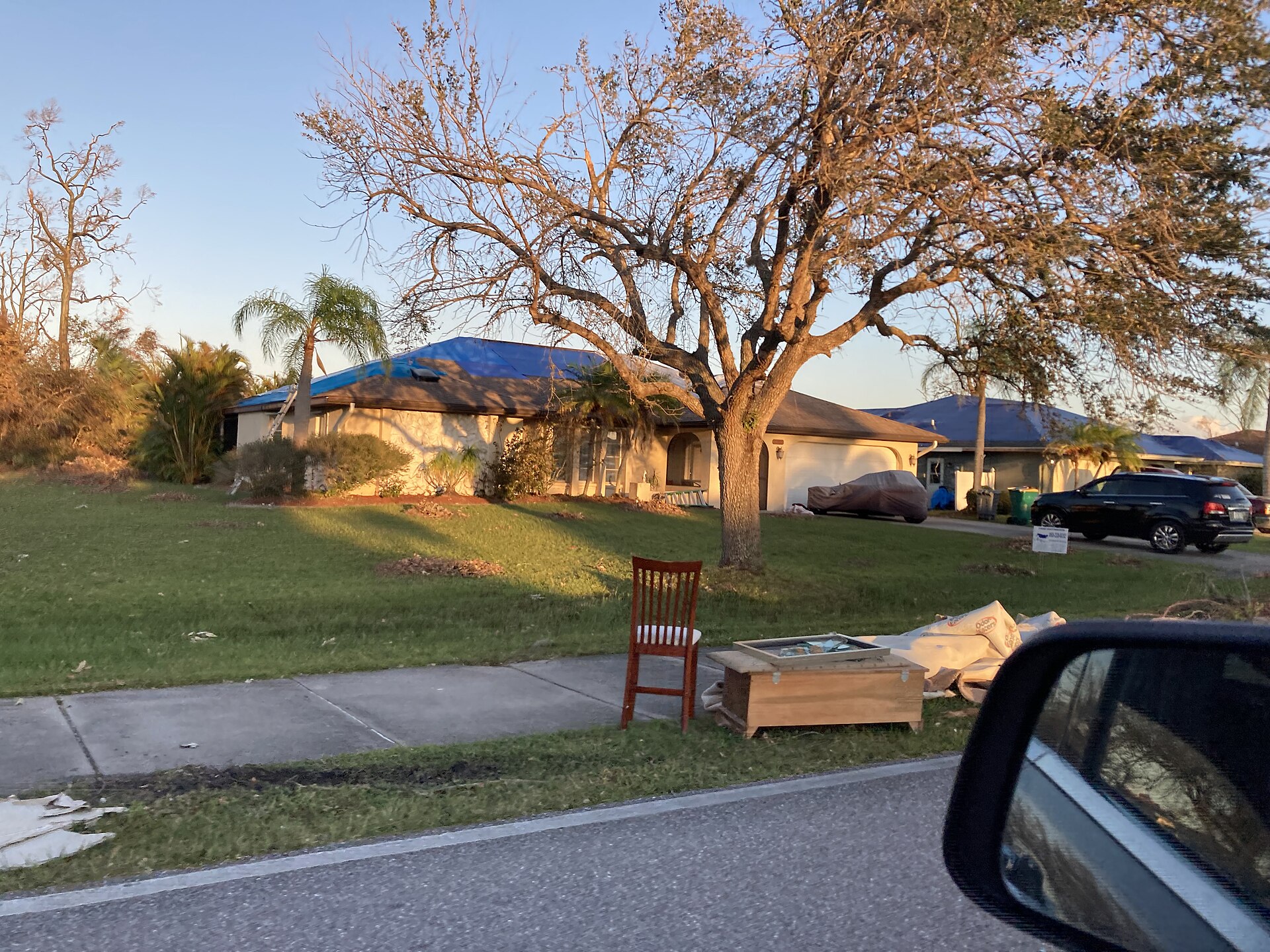 Florida home with blue tarps covering its roof and damaged belongings set out at the curb after Hurricane Ian