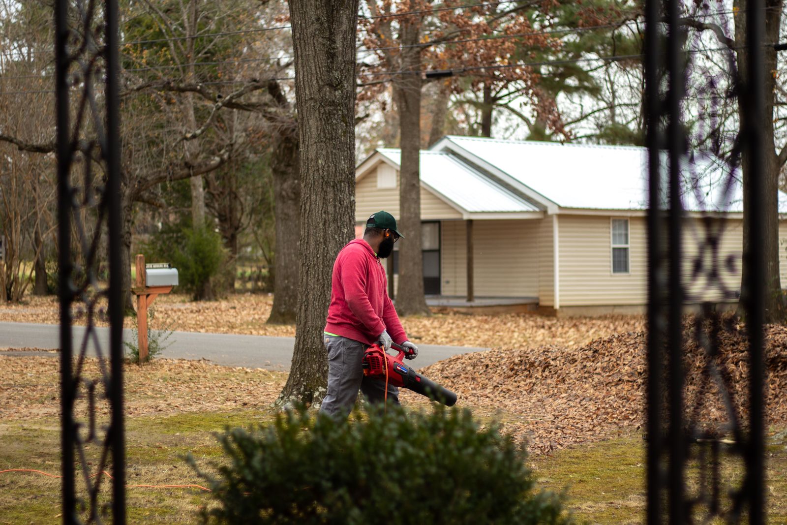 Homeowner using a leaf blower to clear dry leaves from a yard in front of a house among trees