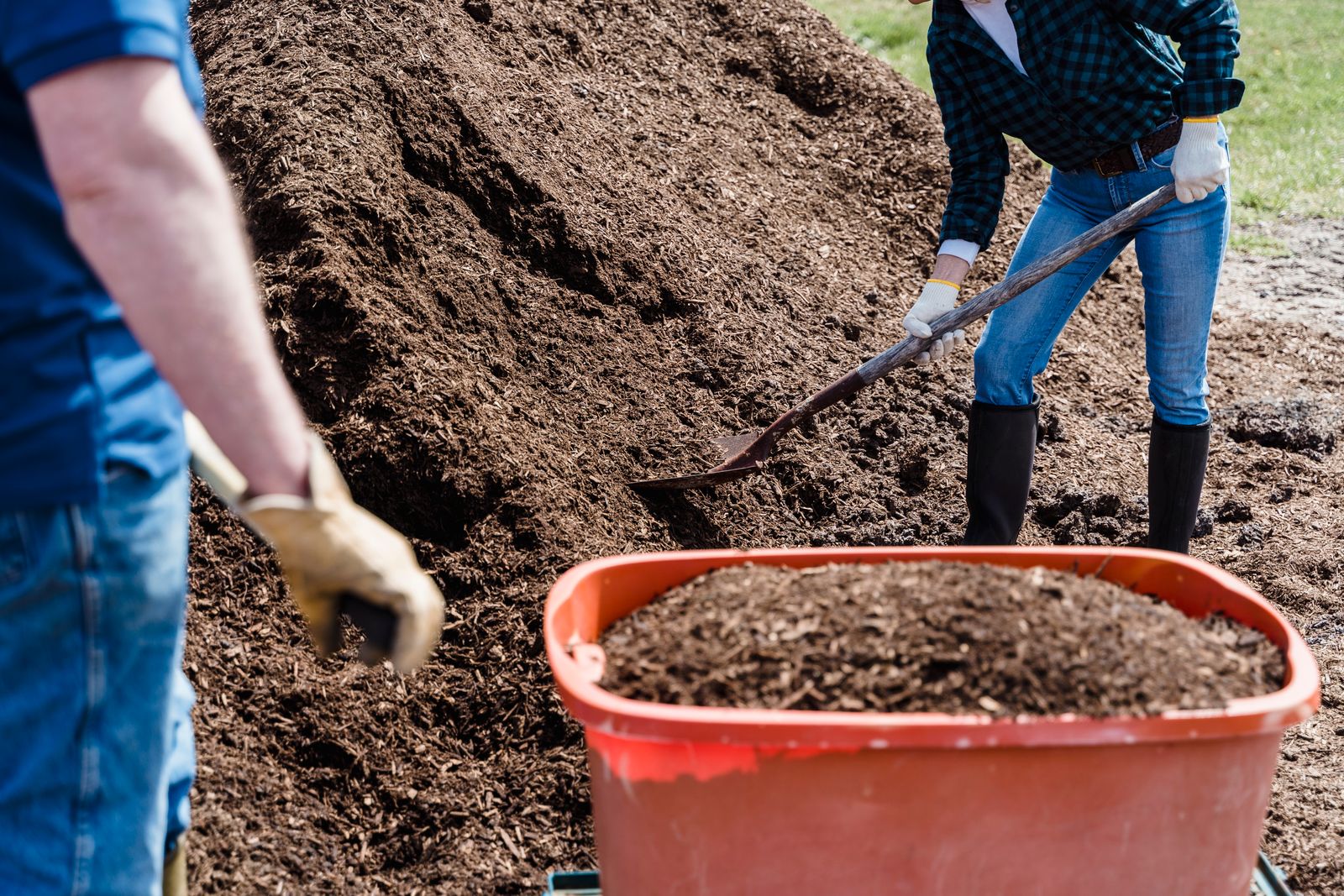 Homeowners shoveling soil into a wheelbarrow to regrade around a home