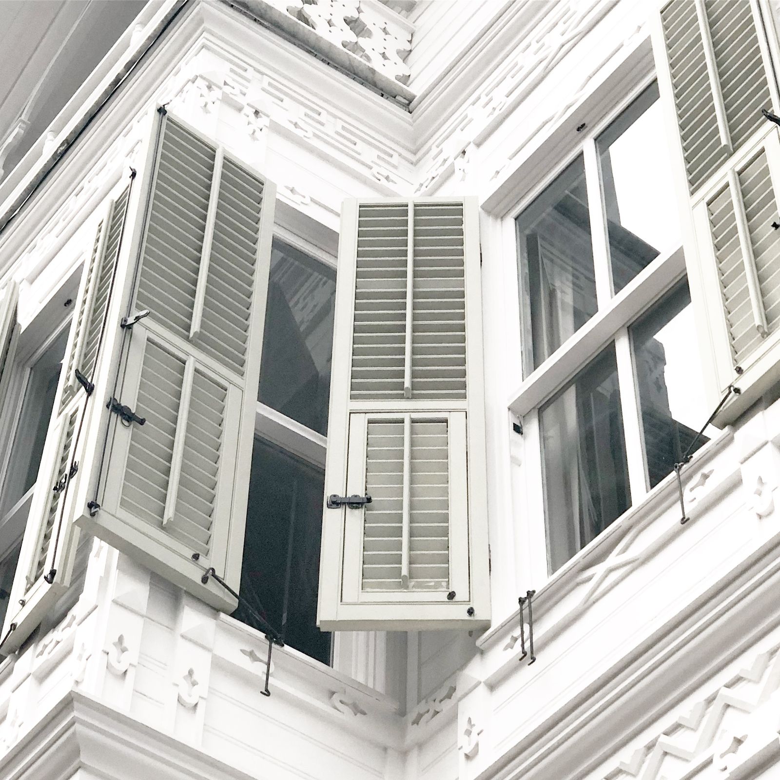 Open louvered colonial-style shutters beside windows on a white home