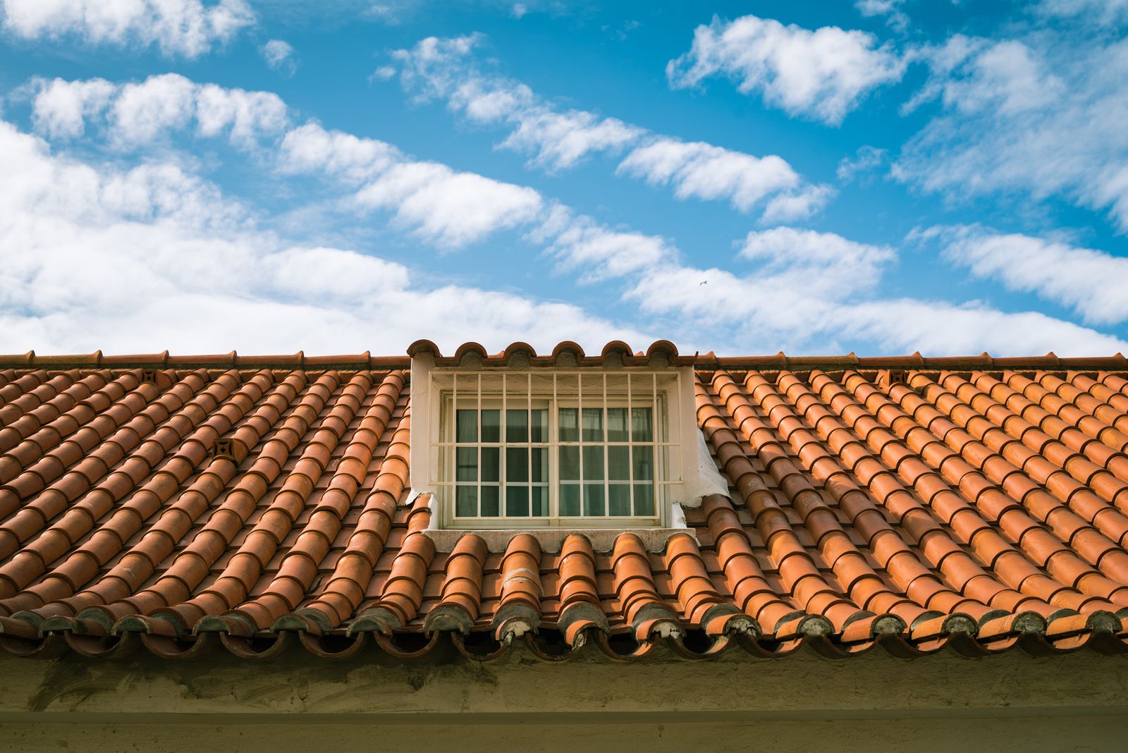 Finished terracotta tile roof with a dormer window under a blue sky
