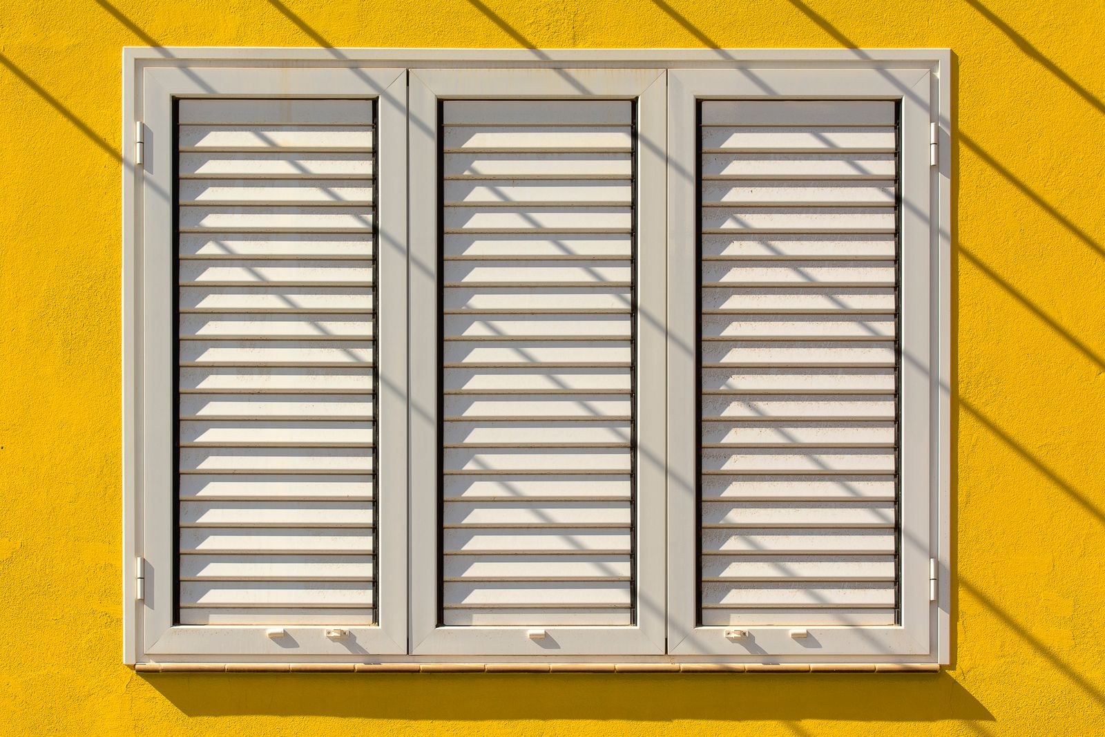 Closed louvered shutters covering a window on a yellow exterior wall