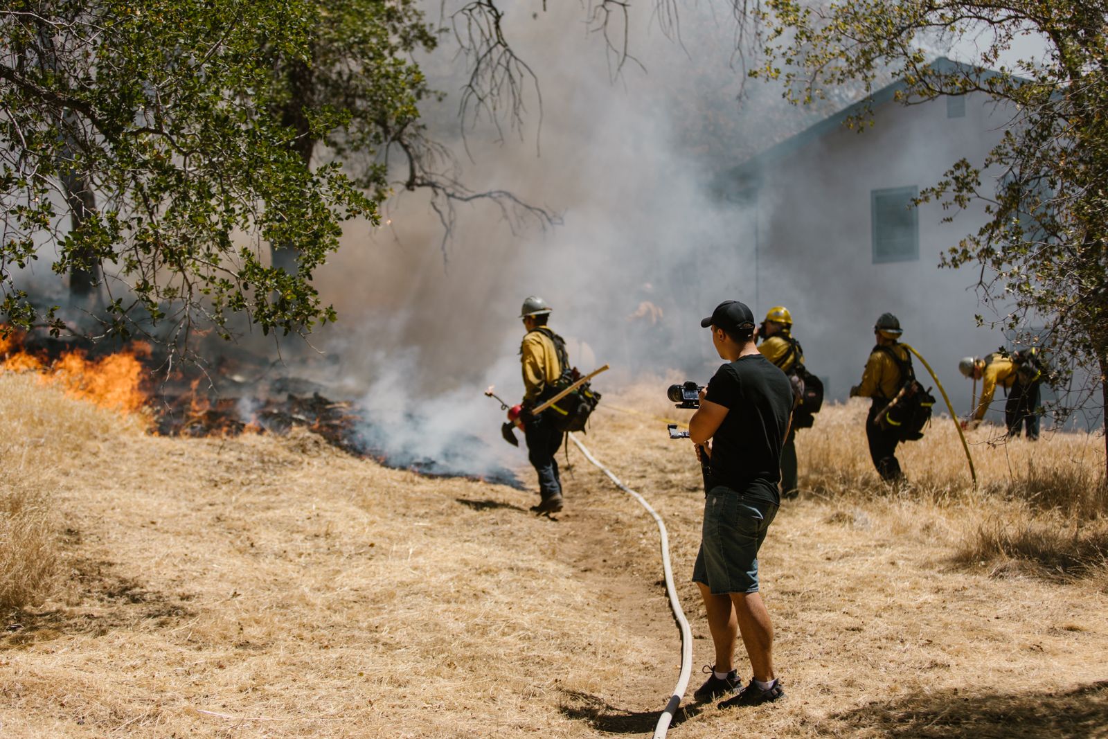 Wildland firefighters working a hose line as a grass fire burns near a home